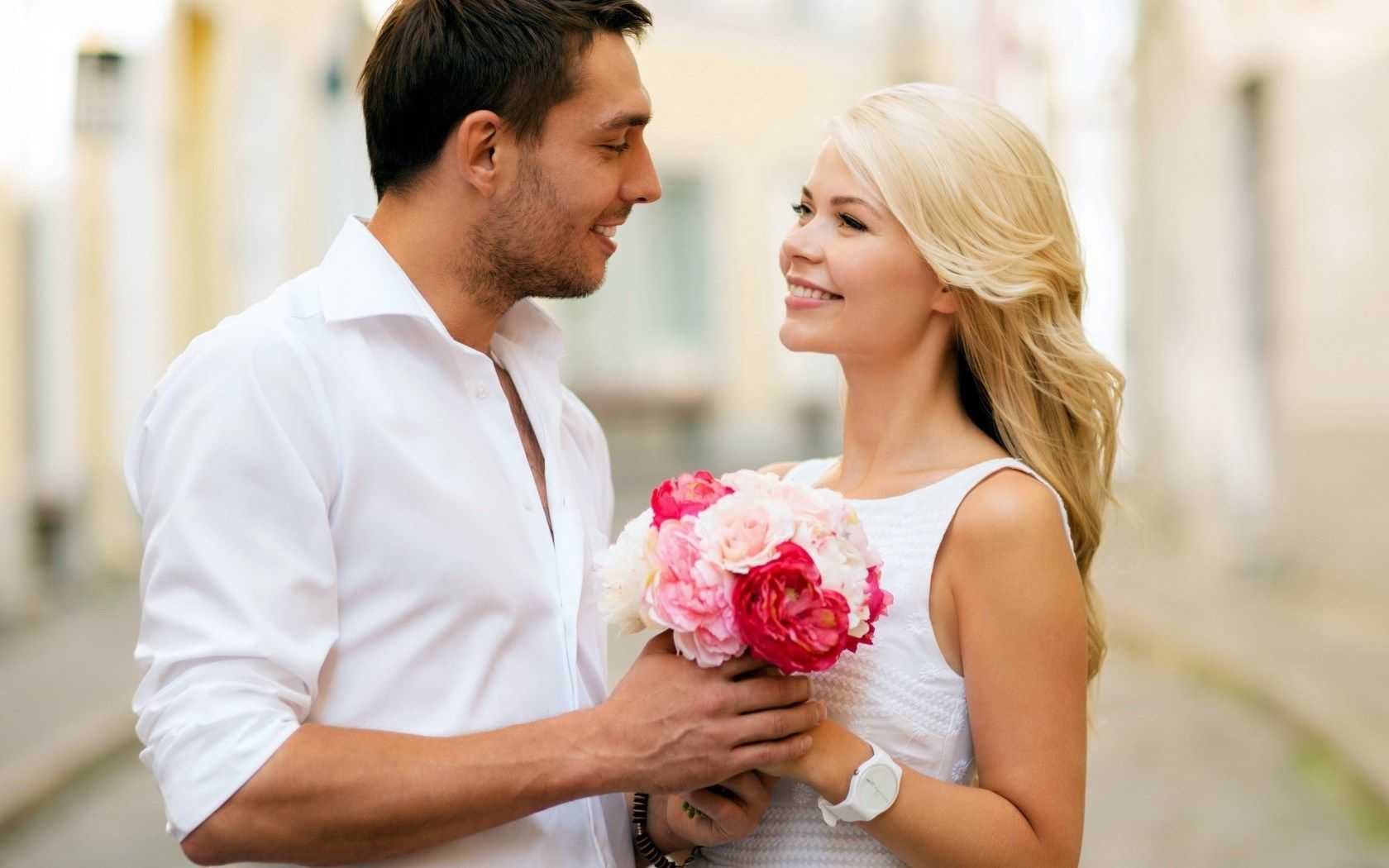 Люб е. Мужчина дарит цветы женщине. Парень дарит девушке цветы. Счастливая женщина. Мужчина и женщина с цветами.